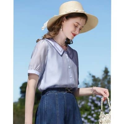 Soft blue blouse with detailed collar, paired with high-waisted jeans, accessorized with pearls and a wide-brim hat for a chic look perfect for sunny days.