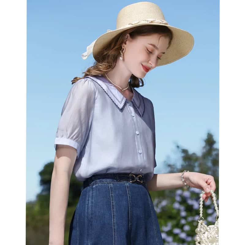 Soft blue blouse with detailed collar, paired with high-waisted jeans, accessorized with pearls and a wide-brim hat for a chic look perfect for sunny days.