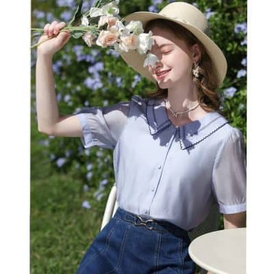 Bright and cheerful woman enjoying sunny day in stylish blouse and wide-brim hat.