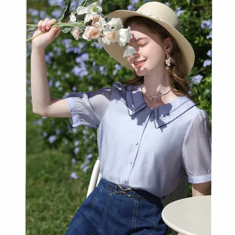 Bright and cheerful woman enjoying sunny day in stylish blouse and wide-brim hat.