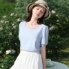 Beautiful woman in light blue blouse, wide-brim hat, enjoying sunny garden. Perfect for outdoor fashion, sun protection, and summer accessories.