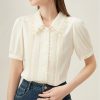 Stylish cream women's blouse featuring delicate lace collar, vertical pleats, and short puff sleeves, perfect for sophisticated fashion and office wear.