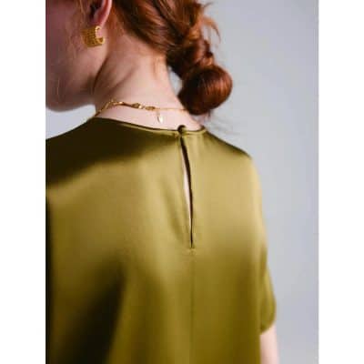 A fashionable gold blouse featuring a back keyhole opening, paired with elegant jewelry, ideal for professional or stylish everyday look.