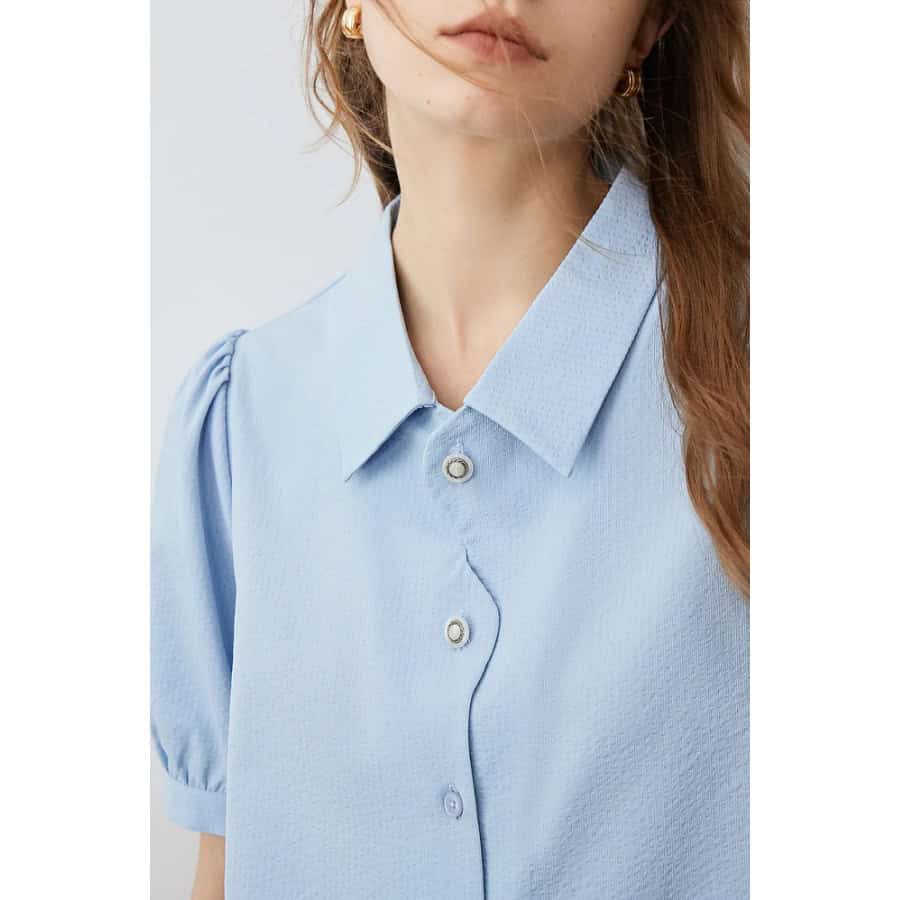 Close-up of a stylish light blue women's blouse with a collar, button-up front, and puffed short sleeves. Perfect for professional and casual wear, featuring premium fabric for comfort and style.