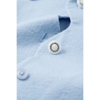 Stylish pearl button on light blue shirt, perfect for enhancing professional or casual outfits. High-quality pearl with metallic accents for a sophisticated look.