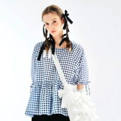 Young girl wearing stylish blue checkered dress with black ribbons in her hair, carrying a white woven bag. Perfect for kids' eyewear fashion and accessories from Monalisa Medical Store.