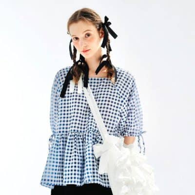 Young girl wearing stylish blue checkered dress with black ribbons in her hair, carrying a white woven bag. Perfect for kids' eyewear fashion and accessories from Monalisa Medical Store.