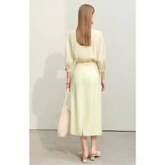 A woman in a stylish beige skirt and top, holding a woven tote bag, showcasing luxury fashion and elegant style for women.