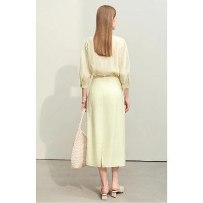 A woman in a stylish beige skirt and top, holding a woven tote bag, showcasing luxury fashion and elegant style for women.