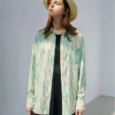 Young woman wearing a pastel tie-dye button-up shirt and wide-brim hat, showcasing fashionable eyewear and summer accessories. Perfect for casual or summer outings.