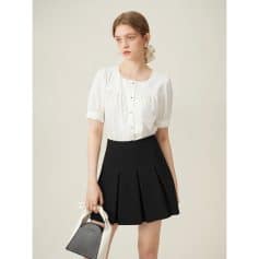 Beautiful young woman wearing elegant white blouse and pleated black skirt, holding a chic bag, perfect for professional and casual wear, showcasing modern fashion trends at Monalisa Store.