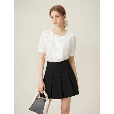 Beautiful young woman wearing elegant white blouse and pleated black skirt, holding a chic bag, perfect for professional and casual wear, showcasing modern fashion trends at Monalisa Store.