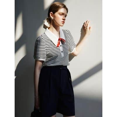 Elegant fashion photograph featuring a young woman in a striped blouse with a red bow, stylish navy shorts, and accessories, showcasing trendy women's clothing at Monalisa Store.