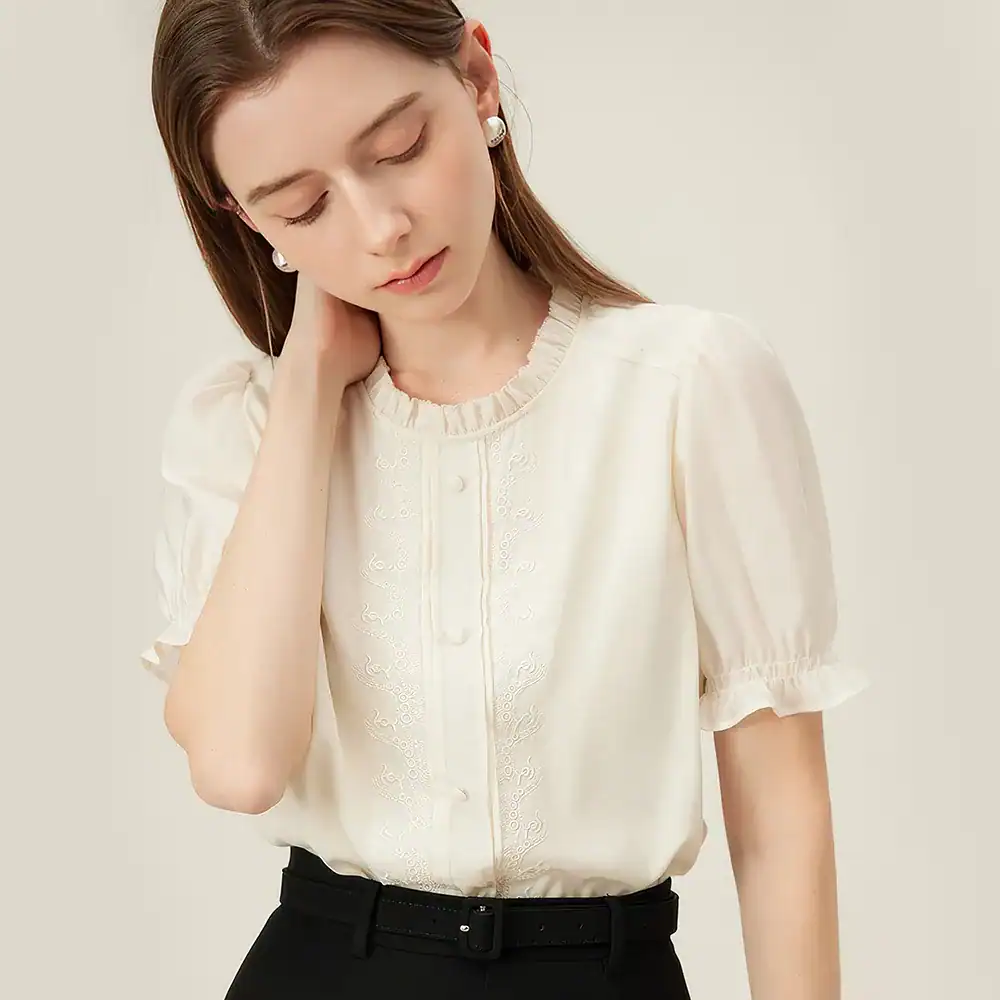 Beautiful white women's blouse with delicate embroidery, short puff sleeves, and a ruffled neckline, perfect for office or casual outings.