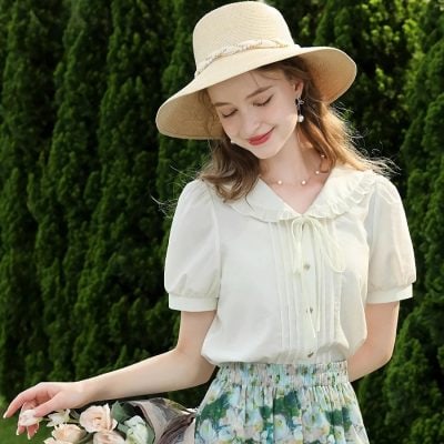 Beautiful woman wearing a cream-colored vintage blouse, floral skirt, and wide-brimmed hat, enjoying a sunny day outdoors. Perfect for spring and summer fashion, casual outings, and garden parties.