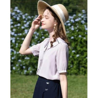 Elegant woman wearing sun hat and stylish sunglasses in outdoor setting with lush greenery background.