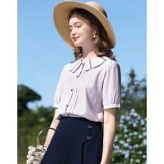 A stylish woman enjoying a sunny day, wearing a chic short-sleeve blouse, wide-brim hat, and butterfly-embellished skirt, showcasing fashionable summer clothing suitable for outdoor activities.