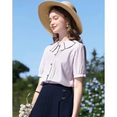 A stylish woman enjoying a sunny day, wearing a chic short-sleeve blouse, wide-brim hat, and butterfly-embellished skirt, showcasing fashionable summer clothing suitable for outdoor activities.