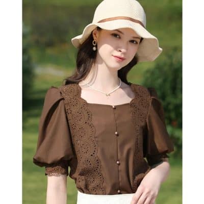 A stylish woman in a brown embroidered blouse and cream hat enjoying a sunny day.