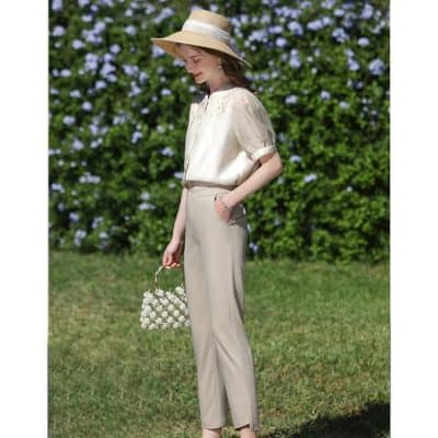 Stylish summer fashion for women featuring a chic wide-brim hat, light beige blouse, tailored beige trousers, and a floral accessory, perfect for outdoor outings or garden events.