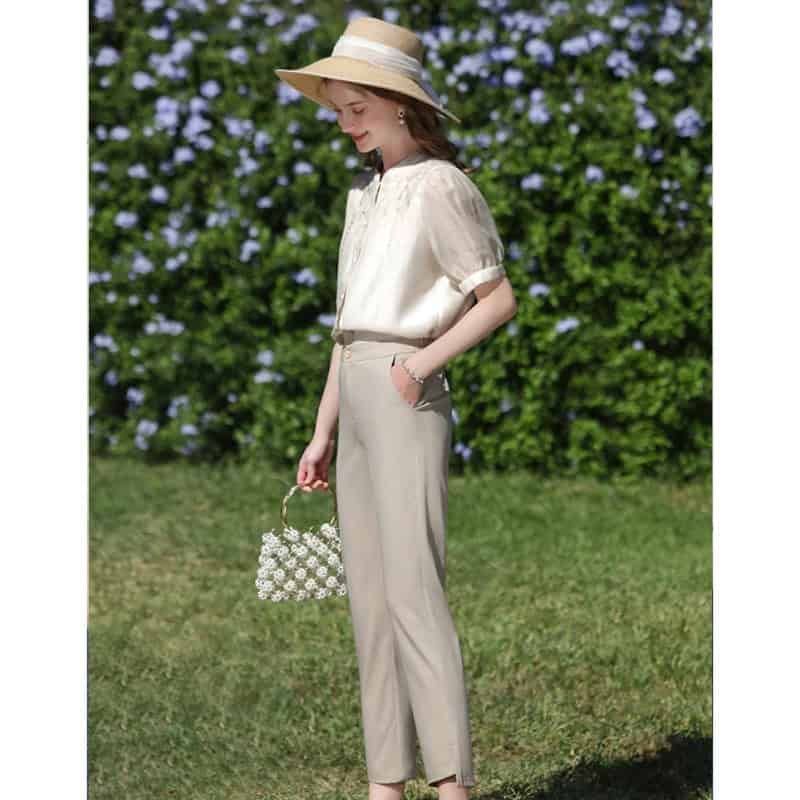Stylish summer fashion for women featuring a chic wide-brim hat, light beige blouse, tailored beige trousers, and a floral accessory, perfect for outdoor outings or garden events.