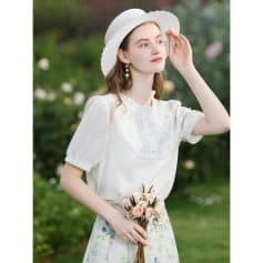 Beautiful young woman in white dress and hat holding pink roses, outdoor fashion, floral accessories, summer style, garden setting.