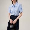 Elegant woman in a light blue blouse and navy trousers, holding a black handbag. Perfect for professional and office wear, emphasizing fashion and sophistication.