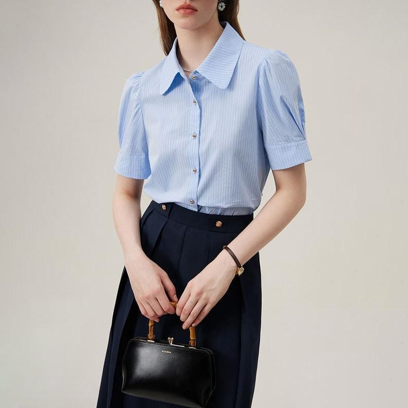 Elegant woman in a light blue blouse and navy trousers, holding a black handbag. Perfect for professional and office wear, emphasizing fashion and sophistication.