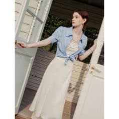 Young woman in stylish blue top and white skirt opening door, showcasing spring fashion and accessories from Monalisa Store.