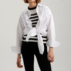 A stylish woman wearing a white tie-front shirt layered over a black and white striped top, paired with black pants for a trendy, casual look. Perfect for fashionable everyday wear or smart casual occasions.