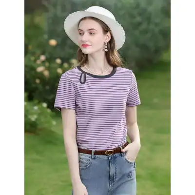 Elegant woman wearing striped top and wide-brim hat, outdoor setting with lush greenery, showcasing trendy casual wear and accessories for a fashionable summer look.