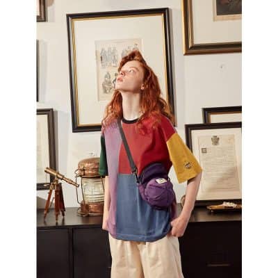 A woman wearing a colorful, stylish color block sweater with a purple crossbody bag, standing in an art-filled space. Perfect for trendy autumn fashion and casual wear.