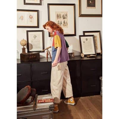 A young woman with red hair showcases trendy casual clothing inside Monalisa Medical Store, surrounded by framed artwork and antique decor, highlighting stylish apparel options available for opt-focused fashion.