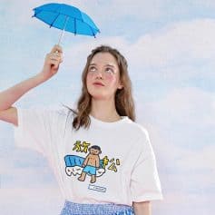A young woman holding a small blue umbrella against a sky background, showcasing a casual fashion style with a graphic tee. Ideal for eyewear promotion, sunglasses, and optical accessories.