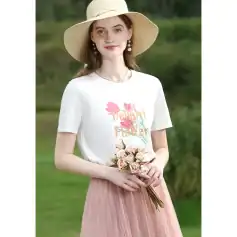 Beautiful young woman wearing a white graphic T-shirt with "Delight Flower" print, pink pleated skirt, and large sun hat, holding a bouquet of roses outdoors.