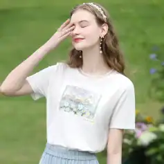 Young woman wearing stylish jewelry and a white graphic t-shirt, outdoors in a lush garden, showcasing Monalisa Medical optic accessories and fashionable eyewear.