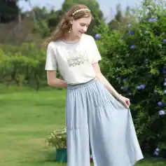 Effortless chic style with white printed t-shirt and flowy light blue pants showcased outdoors, ideal for women’s fashion shoppers.