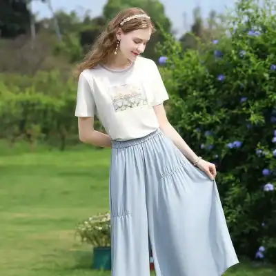 Effortless chic style with white printed t-shirt and flowy light blue pants showcased outdoors, ideal for women’s fashion shoppers.