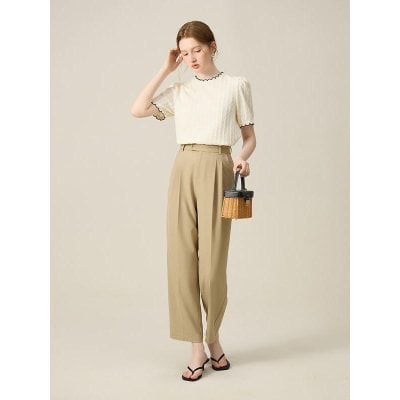 A stylish woman dressed in a light-colored blouse and beige high-waisted trousers, holding a small wicker handbag. Perfect for office, casual outings, and summer fashion.