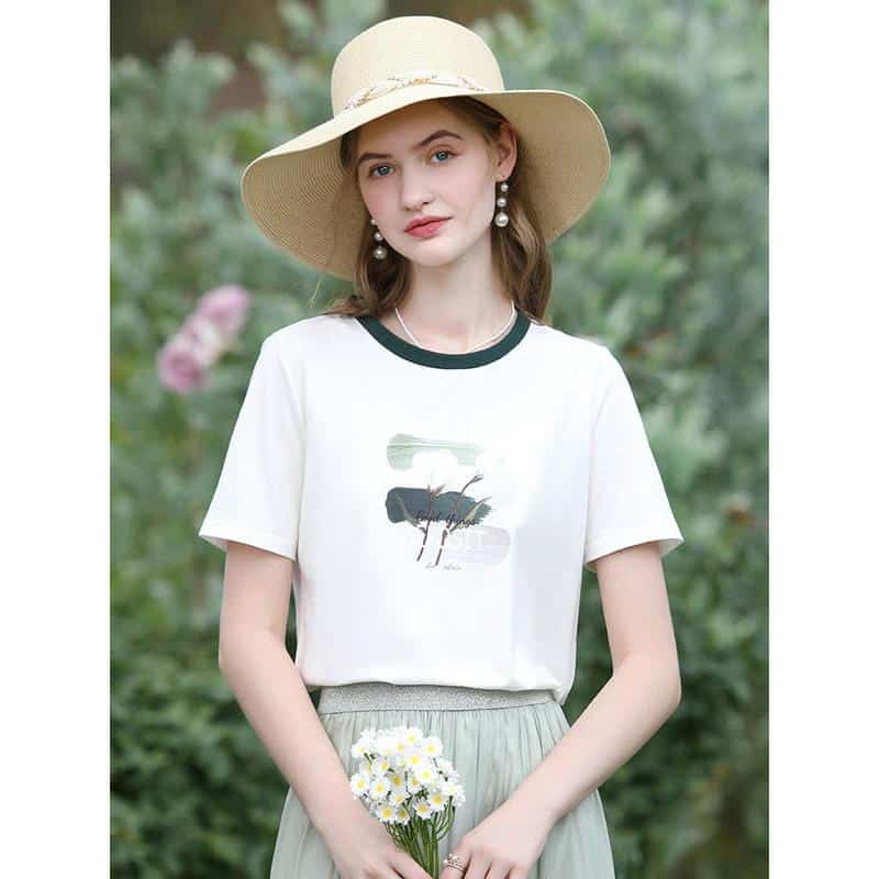 Beautiful young woman wearing wide-brimmed hat, casual white T-shirt with nature graphic, stylish earrings, holding a small bouquet of daisies outdoors, showcasing fashionable and comfortable summer look.