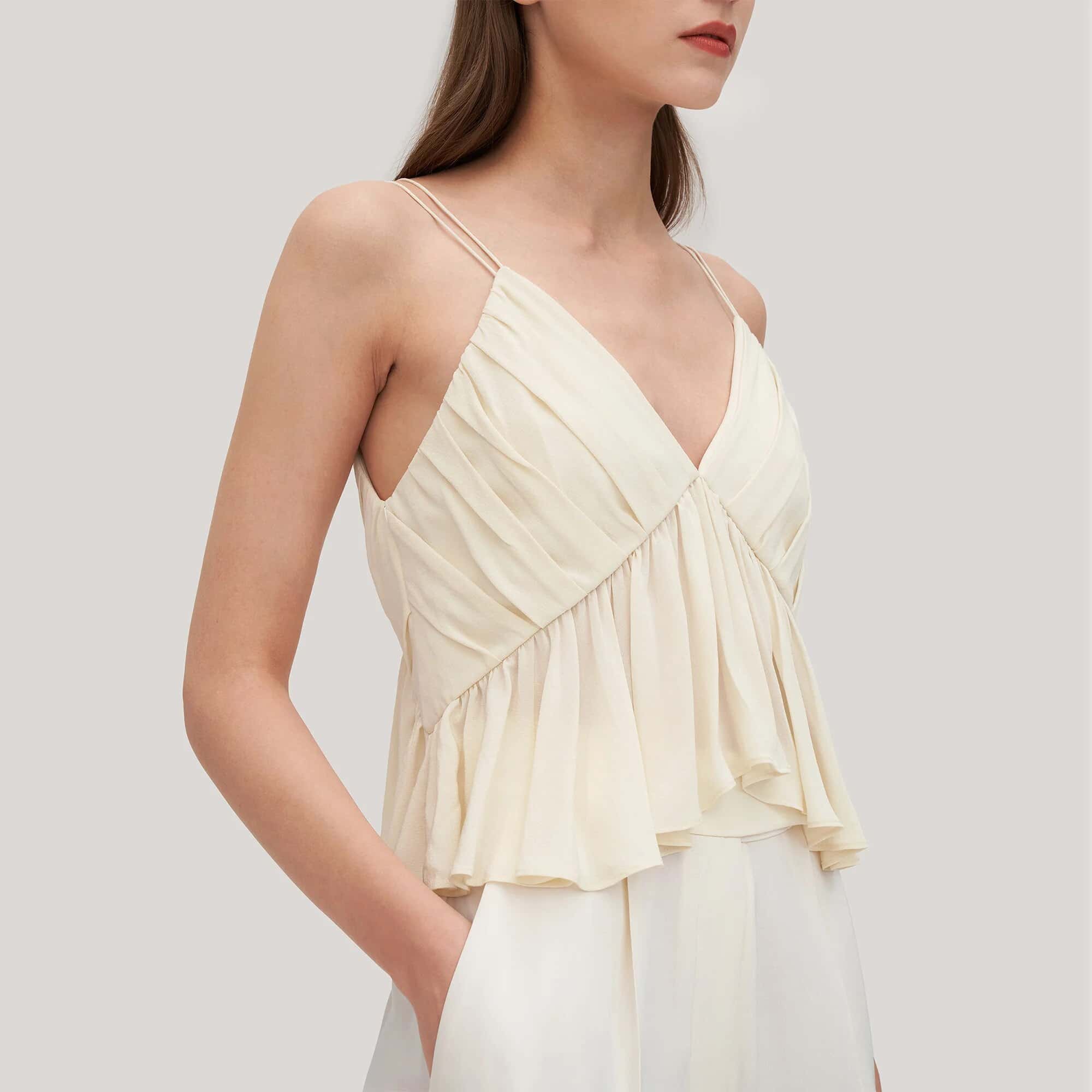 A stylish women’s cream-colored tank top with delicate spaghetti straps, a V-neckline, and a ruffled hem for a fashionable, feminine look, perfect for casual or summer wear.