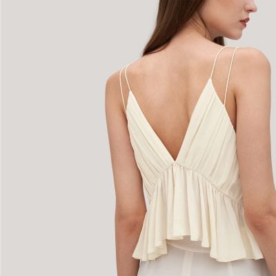 Stylish cream-colored sleeveless top featuring a deep V-back, lightweight fabric, pleated detailing, and ruffled hem perfect for summer fashion and casual wear.