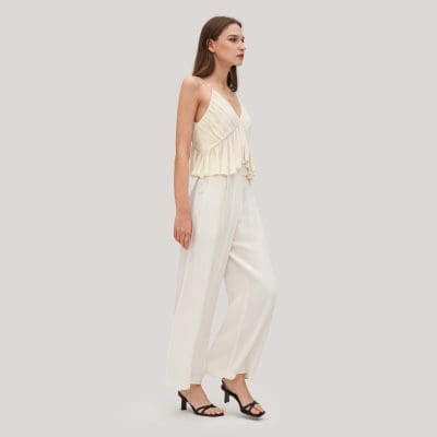 A stylish woman wearing a cream-colored, layered, sleeveless top with wide-leg trousers, perfect for modern fashion. She is dressed in chic, elegant clothing suited for casual or semi-formal occasions.
