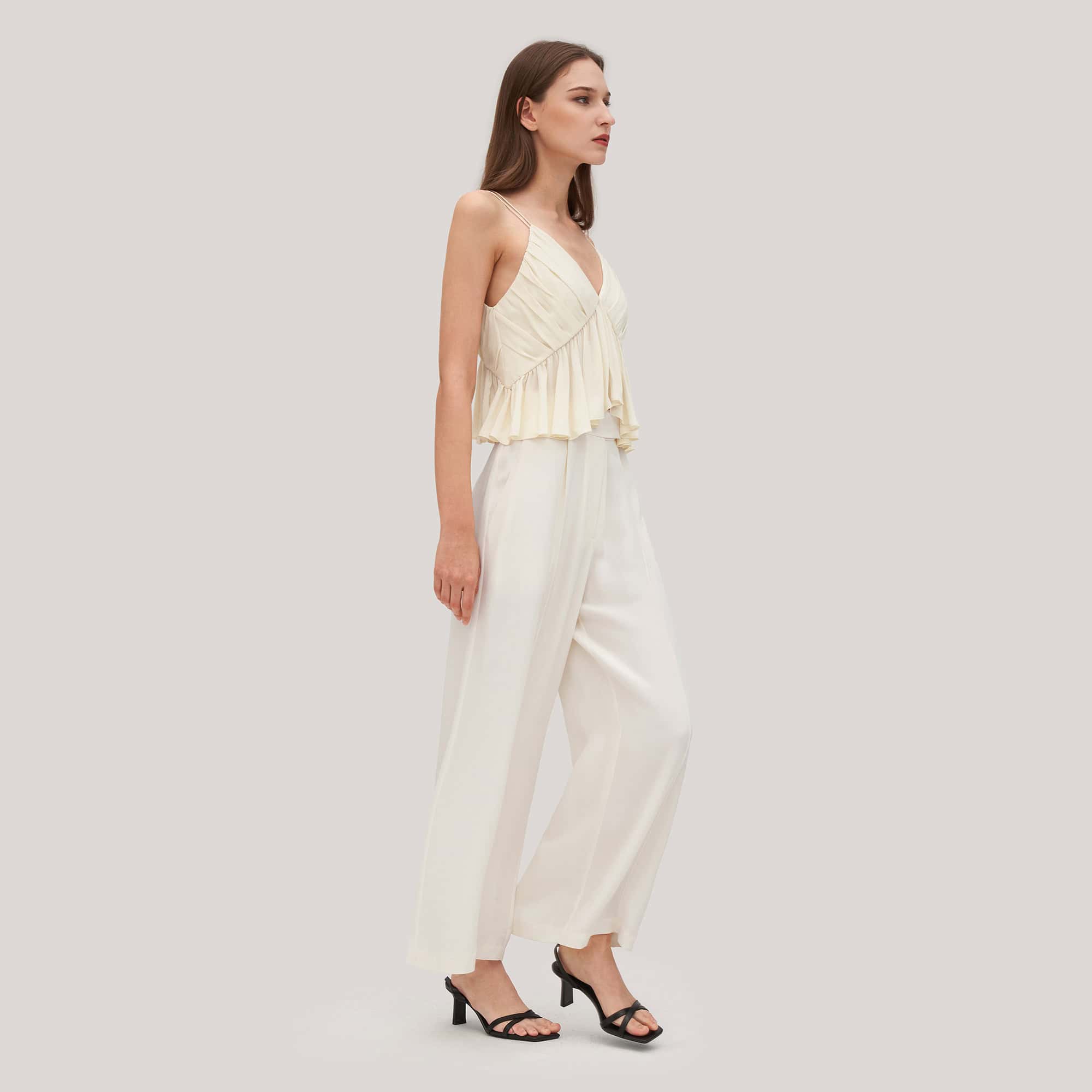 A stylish woman wearing a cream-colored, layered, sleeveless top with wide-leg trousers, perfect for modern fashion. She is dressed in chic, elegant clothing suited for casual or semi-formal occasions.