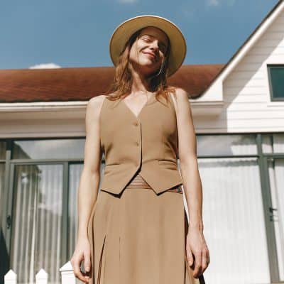 Chic woman in beige vest and skirt with wide-brim hat outdoors, emphasizing trendy summer fashion, accessories, and stylish looks for all seasons.