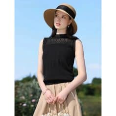 Stylish black sleeveless top with pleated details, paired with a beige skirt, wide-brim straw hat, and jewelry—perfect for chic summer looks and outdoor fashion statements.