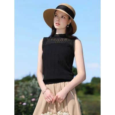 Stylish black sleeveless top with pleated details, paired with a beige skirt, wide-brim straw hat, and jewelry—perfect for chic summer looks and outdoor fashion statements.