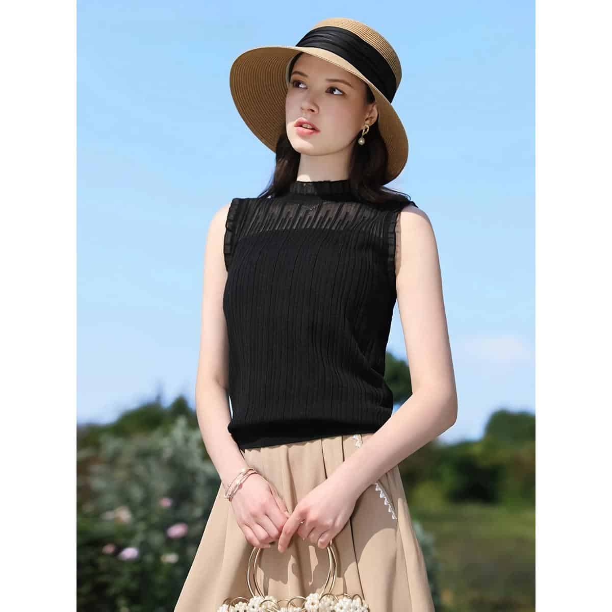 Stylish black sleeveless top with pleated details, paired with a beige skirt, wide-brim straw hat, and jewelry—perfect for chic summer looks and outdoor fashion statements.
