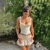 A stylish woman poses outdoors wearing a fitted cream corset with ruffled straps and a matching flared skirt, showcasing fashion suitable for eye health and optical accessories.