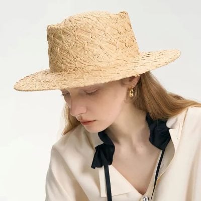 A woman wearing a natural straw hat, perfect for summer sun protection and outdoor fashion, complemented by elegant earrings and a beige blouse with dark accents.